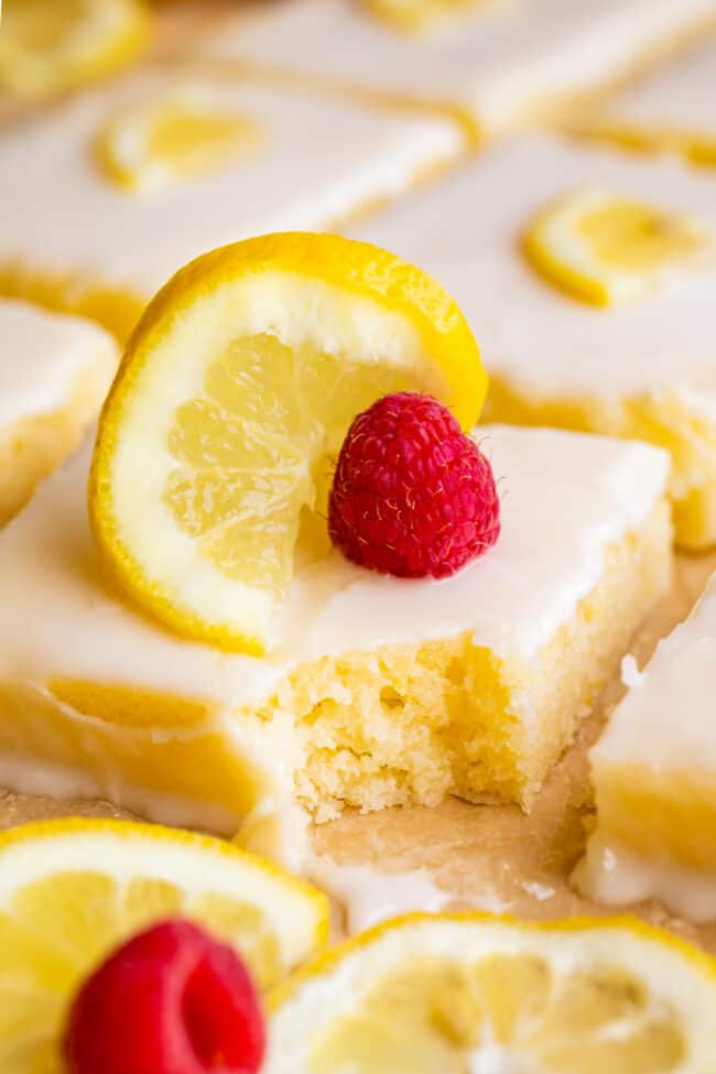 squares of glazed lemon sheet cake with lemon slices and fresh raspberries, a bite missing from one piece.