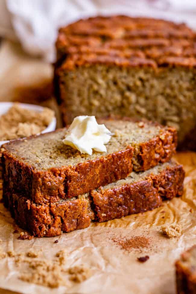 2 slices of super moist banana nut bread with butter on top and a full loaf in the background.