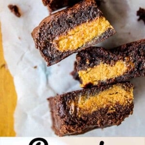 Three thick Reese’s brownies are stacked on parchment paper, each filled with peanut butter cups and sliced to reveal the gooey peanut butter center. Text below reads Reese’s Stuffed Brownies.