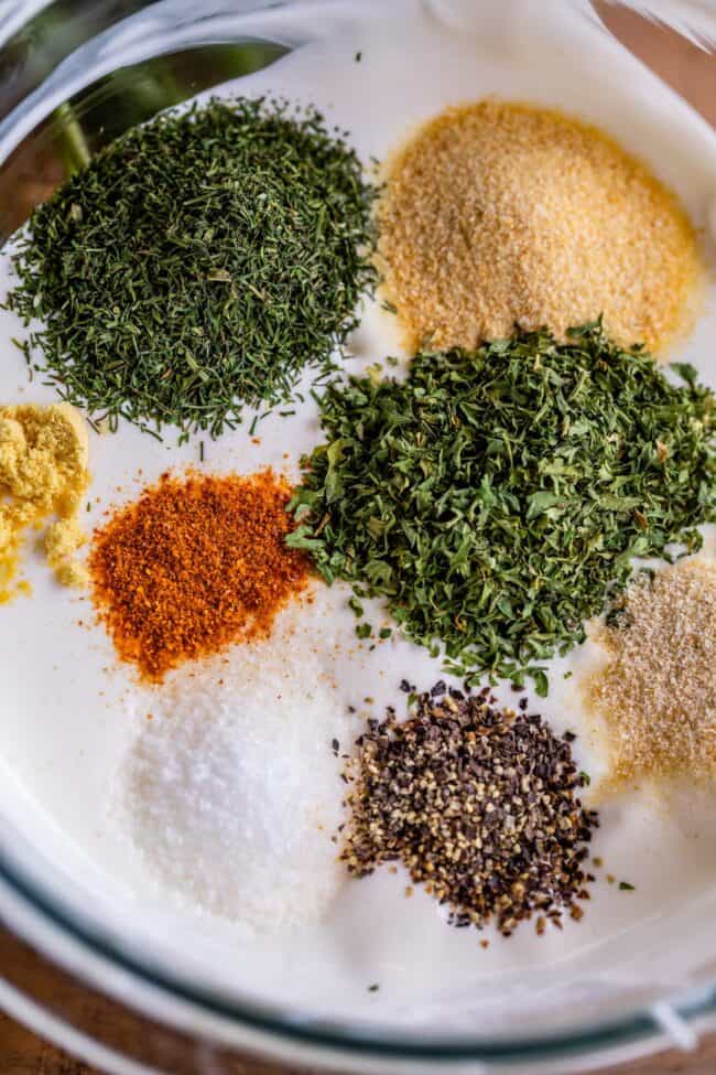 dried herbs being added to creamy buttermilk ranch dressing. 