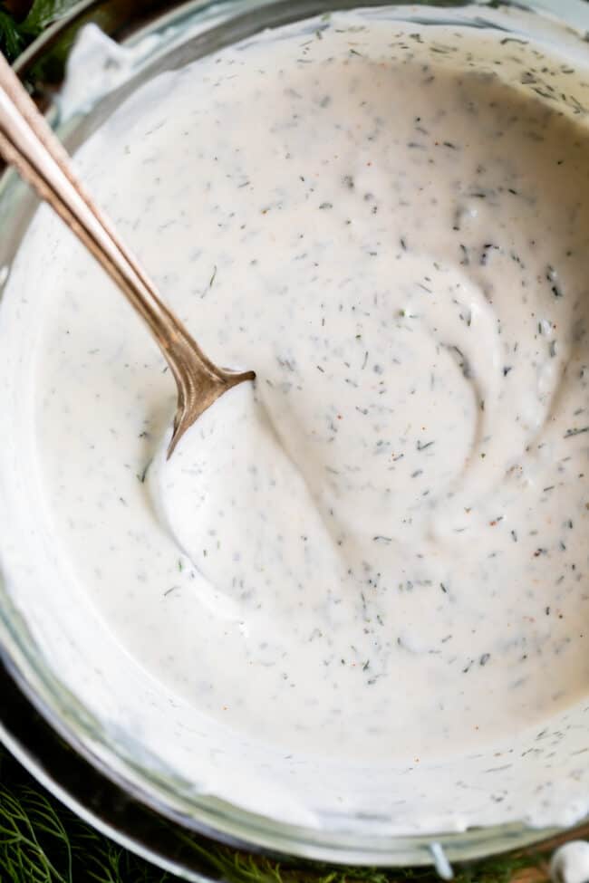 overhead shot of creamy buttermilk ranch dressing in a glass bowl with a spoon in it. 