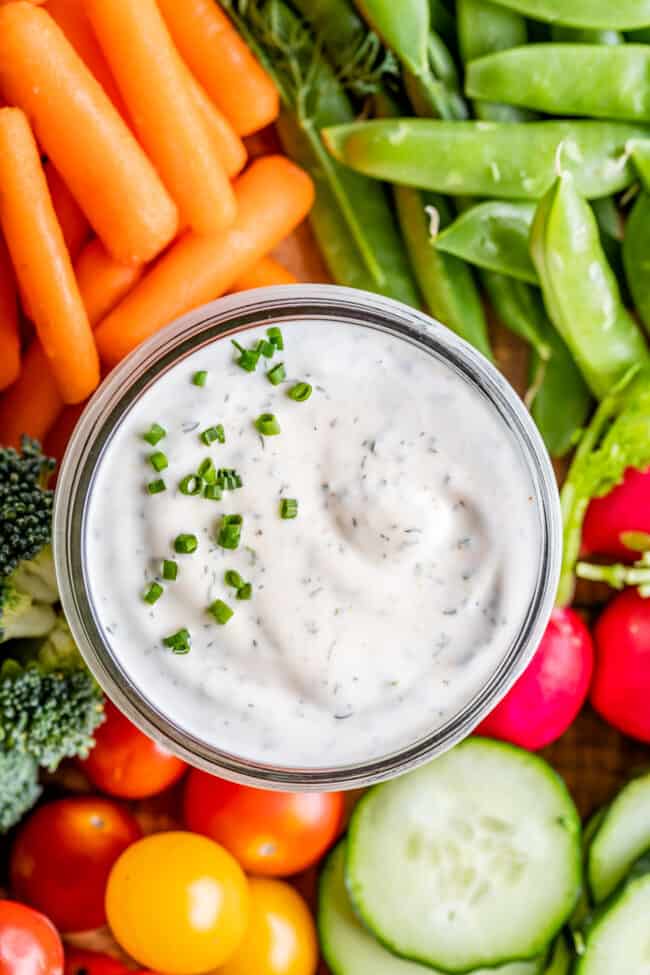 overhead of buttermilk ranch dressing in a glass jar with fresh vegetables surrounding it.