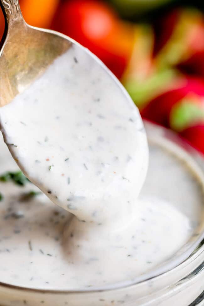 a spoon being dipped into a jar of homemade buttermilk ranch dressing. 