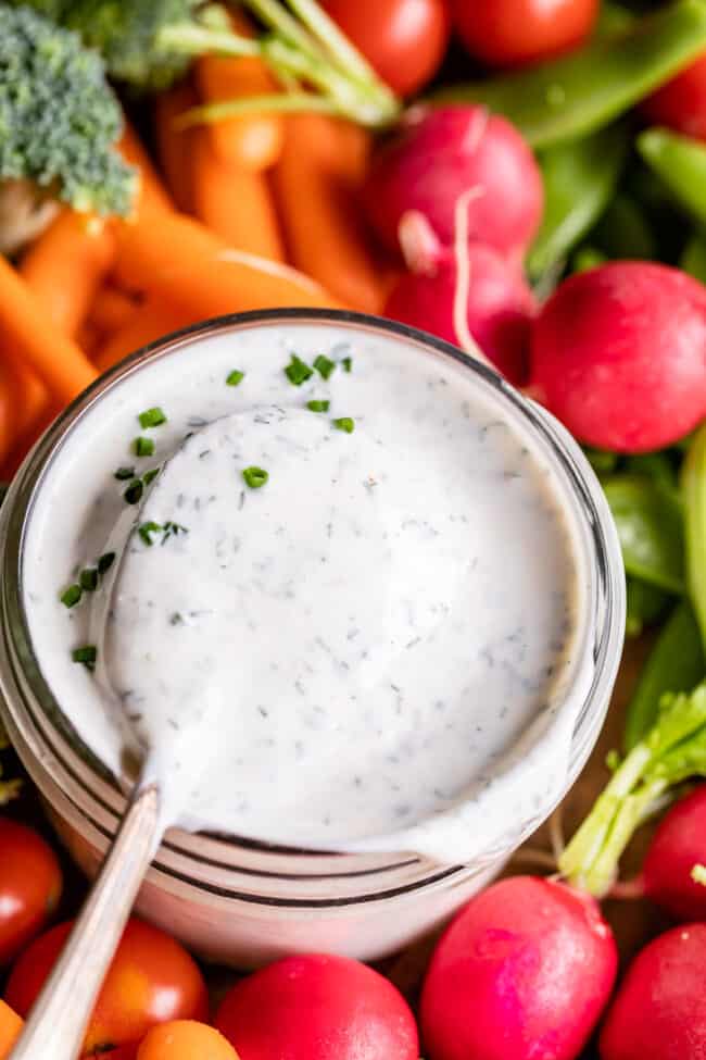 buttermilk ranch dressing in a glass jar surrounded by fresh veggies.