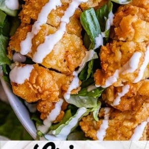 A close-up of crispy chicken salad featuring fried chicken strips on leafy greens with sliced tomatoes, drizzled with buttermilk ranch. Text at the bottom reads Crispy Chicken Salad with Buttermilk Ranch.