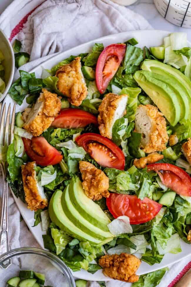 fried chicken salad recipe on a plate with avocados and tomatoes