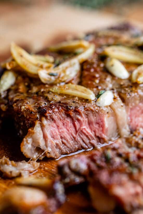 close up of ribeye steak, medium rare, with garlic cloves on top