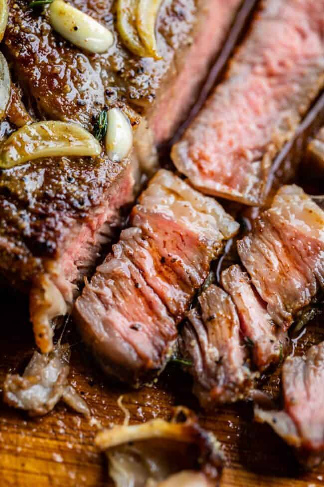 grilled ribeye steak sliced on a cutting board with garlic butter.