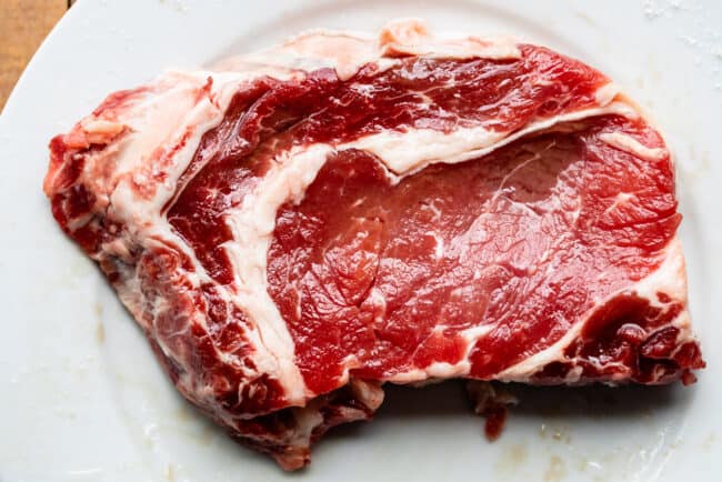 raw ribeye steak on a white plate.