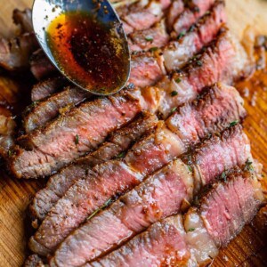 Spoon drizzling brown gravy over bias cut slices of medium rare rib eye steak