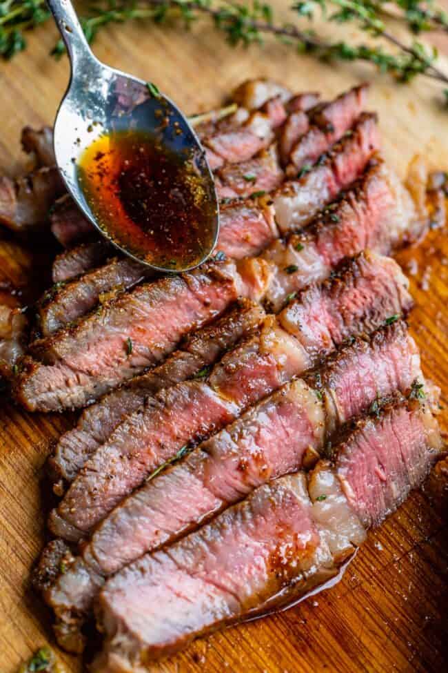 ribeye steak on a cutting board with a spoon of garlic butter.