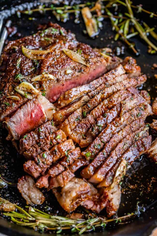 grilled ribeye steak sliced in a pan with garlic butter and fresh herbs.