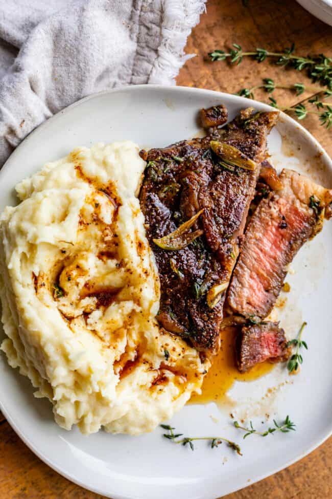 ribeye steak on a plate with mashed potatoes and garlic butter.