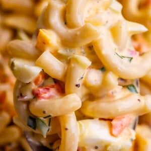 A close-up of a spoonful of creamy macaroni salad with elbow pasta, chopped vegetables, and herbs in a rich, yellow dressing—perfect inspiration for your next macaroni salad.