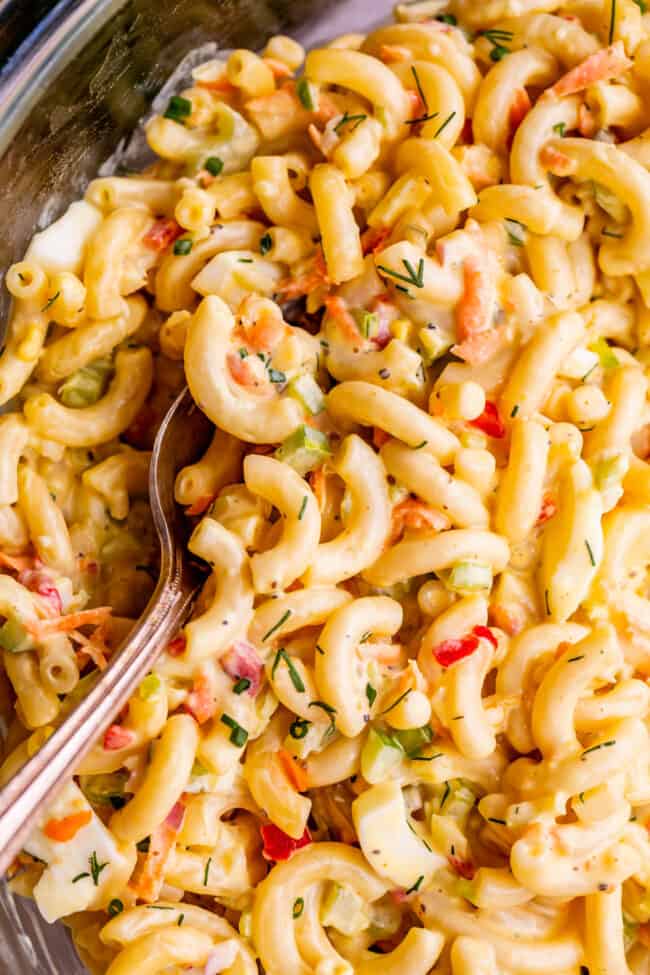 moist macaroni salad in a clear mixing bowl with serving spoon