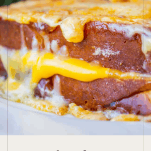 A close-up of a gooey, cheesy grilled cheese sandwich with melted cheese oozing out, served with strawberries in the background. Text on image promotes The Best Grilled Cheese.