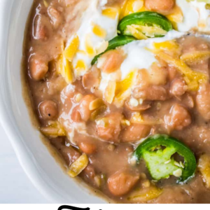 Tejano pinto beans in a bowl with sour cream, cheese, lime, and jalapeno.