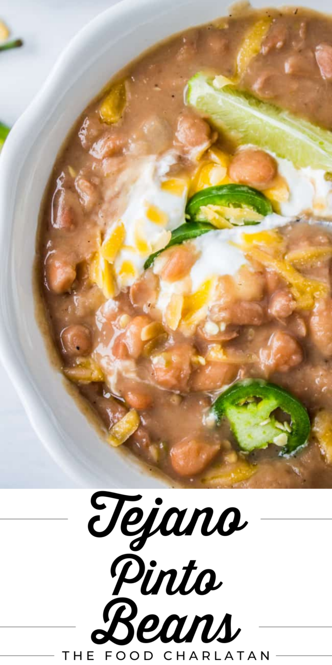 Tejano pinto beans in a bowl with sour cream, cheese, lime, and jalapeno.