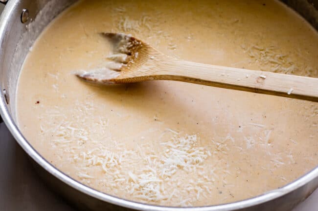 adding parmesan to Alfredo sauce.