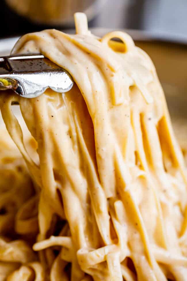 creamy fettuccine in a pan being lifted with tongs.