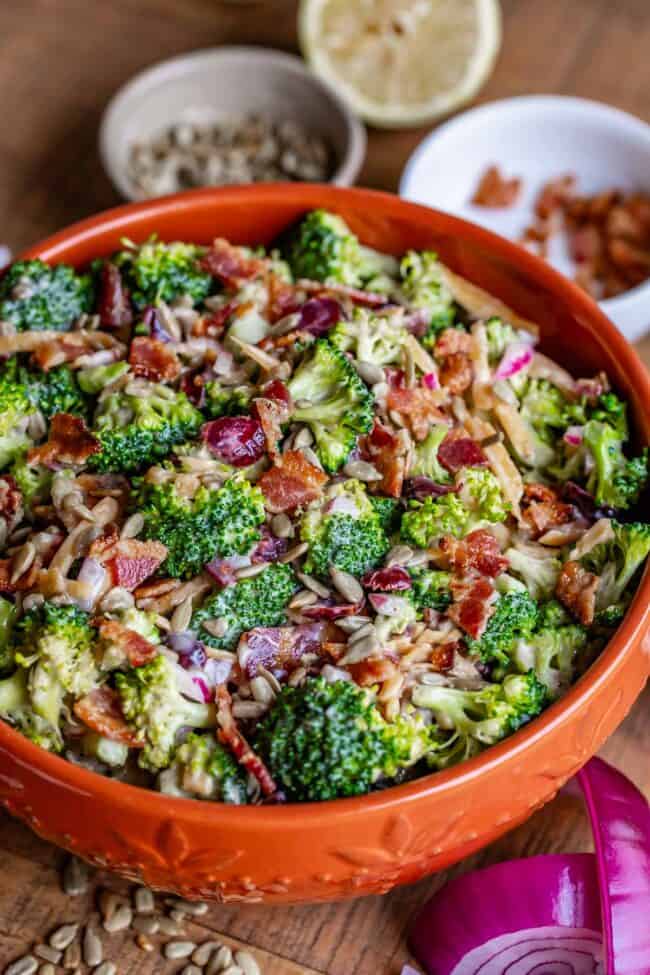 Broccoli and bacon salad in an orange bowl with red onion and a lemon