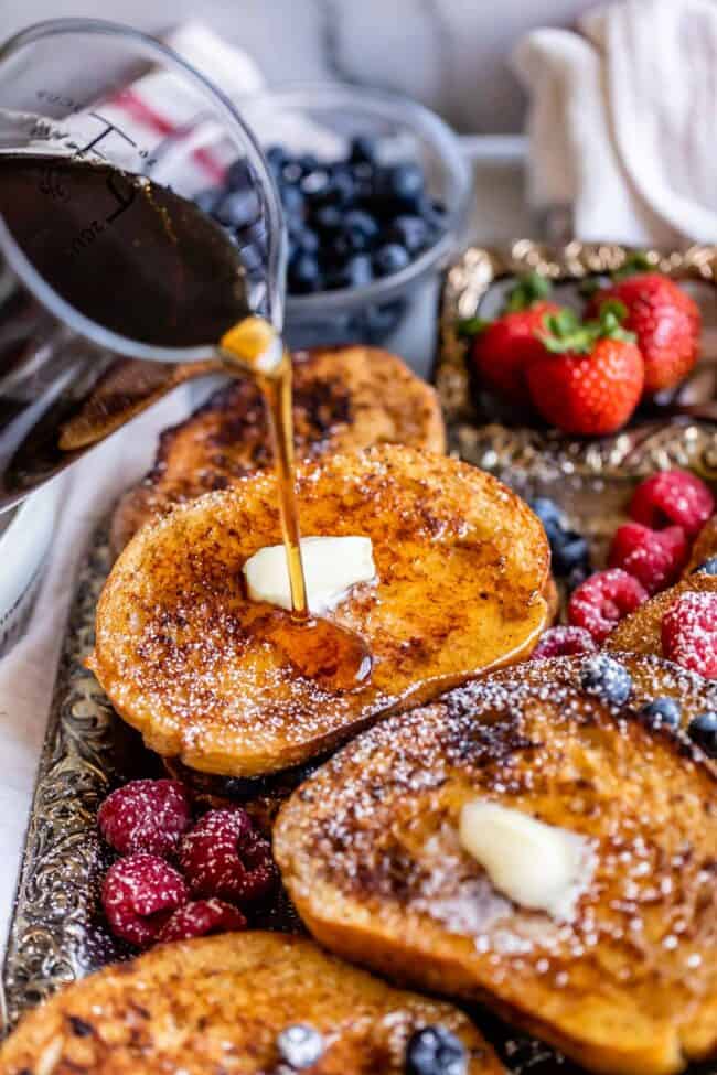 pouring syrup over a tray of brioche french toast.