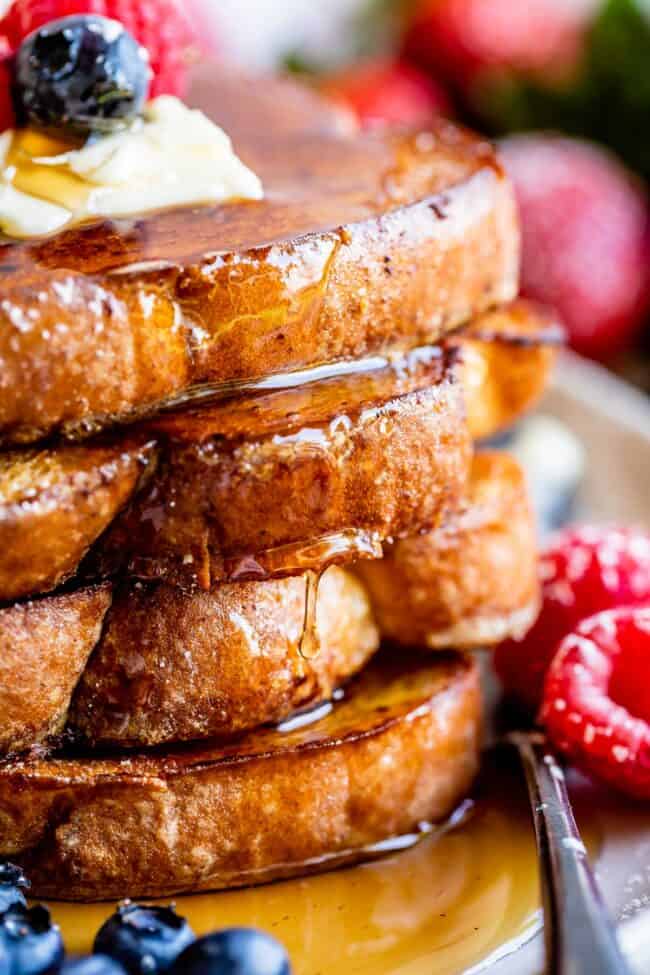 stack of french toast with butter, berries, syrup, and a fork.