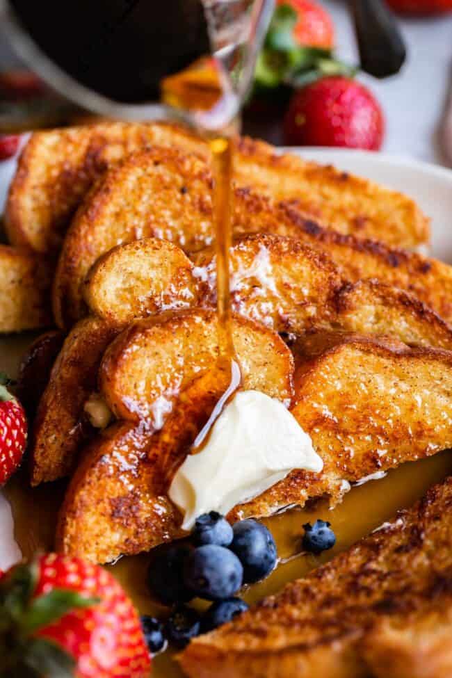 syrup poured over a stack of French toast, with strawberries and blueberries.