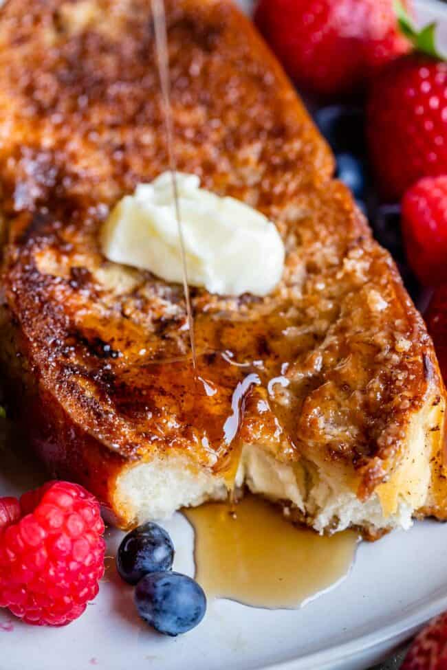 thick french toast on a plate with raspberries, strawberries, blueberries, butter, and syrup.