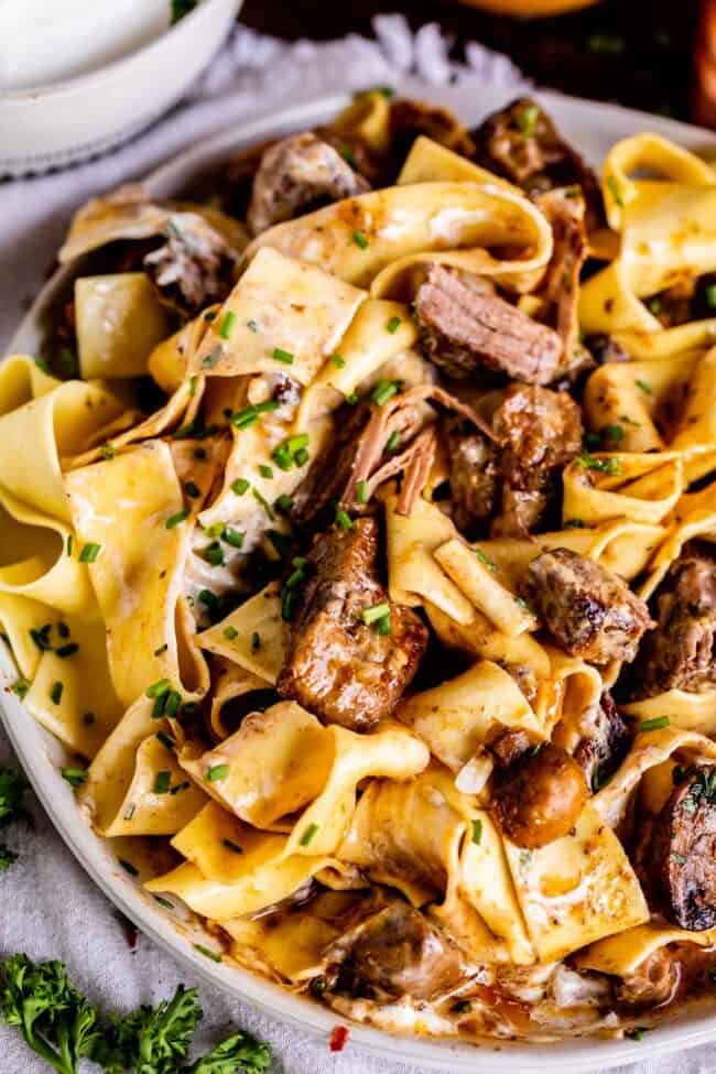 crock pot beef stroganoff served over pappardelle pasta with fresh chives in a bowl.