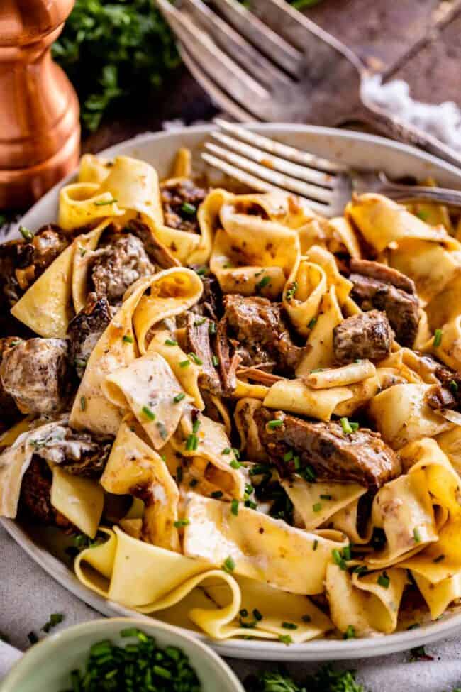 crock pot beef stroganoff served over pappardelle pasta with fresh chives in a bowl with a fork.