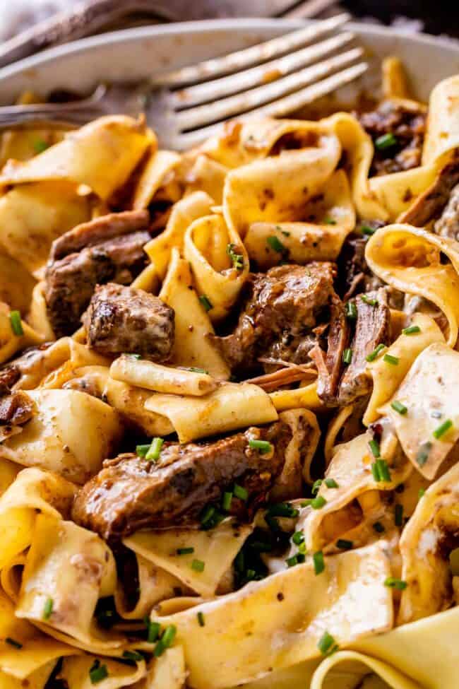crock pot beef stroganoff with fresh chives served over pappardelle pasta with a fork.