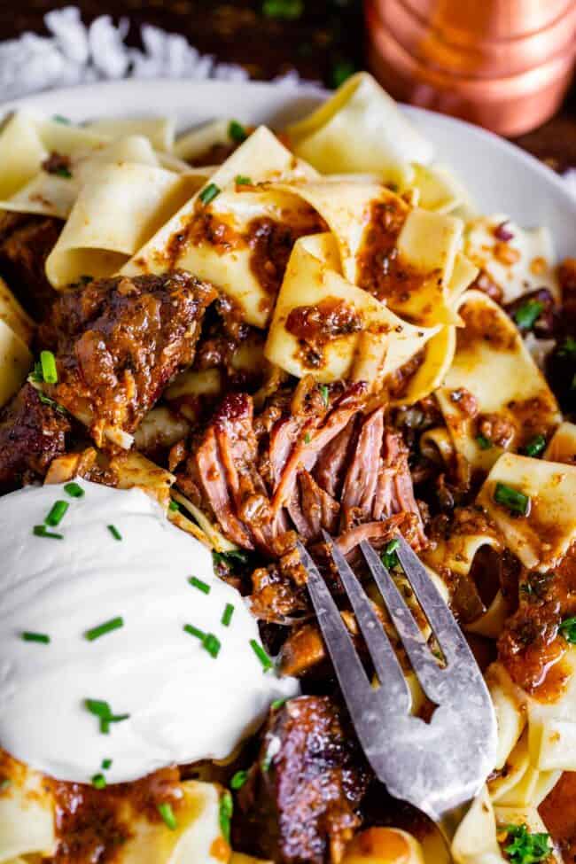 a fork shredding beef from crock pot beef stroganoff with a big dollop of sour cream and fresh chives.