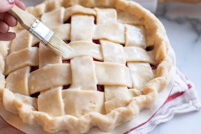 brushing milk and egg on top of lattice pie crust