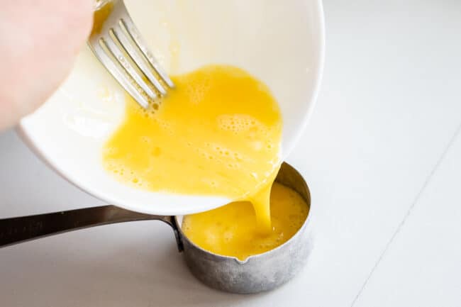 pouring beaten egg into a 1/4 cup measuring cup.