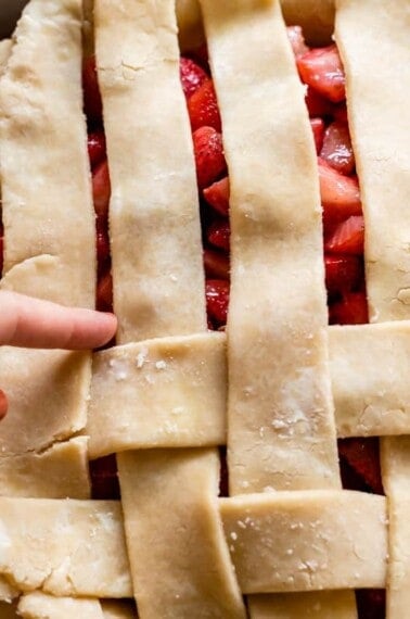 finger pointing to the next strip of pie dough that needs to be pulled back for lattice crust