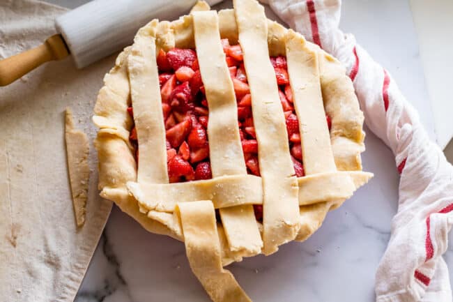 folding back strips of pie dough to make a lattice pie crust on strawberry pie