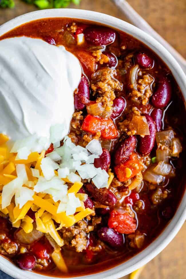 basic chili recipe in a white bowl garnished with sour cream, cheese, onions