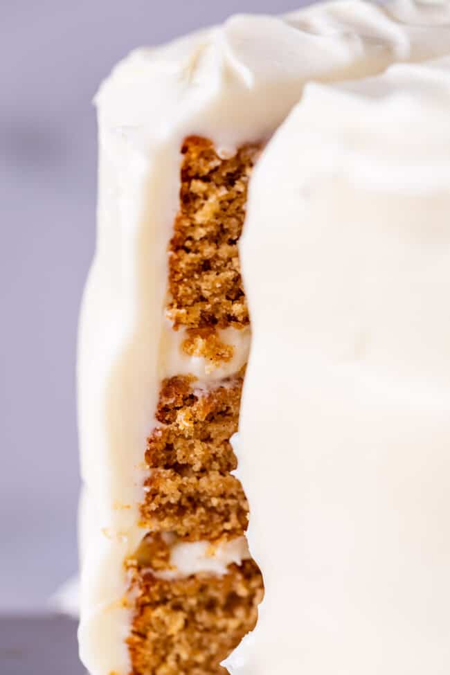 slice of spice cake with cream cheese frosting being lifted from a whole cake.