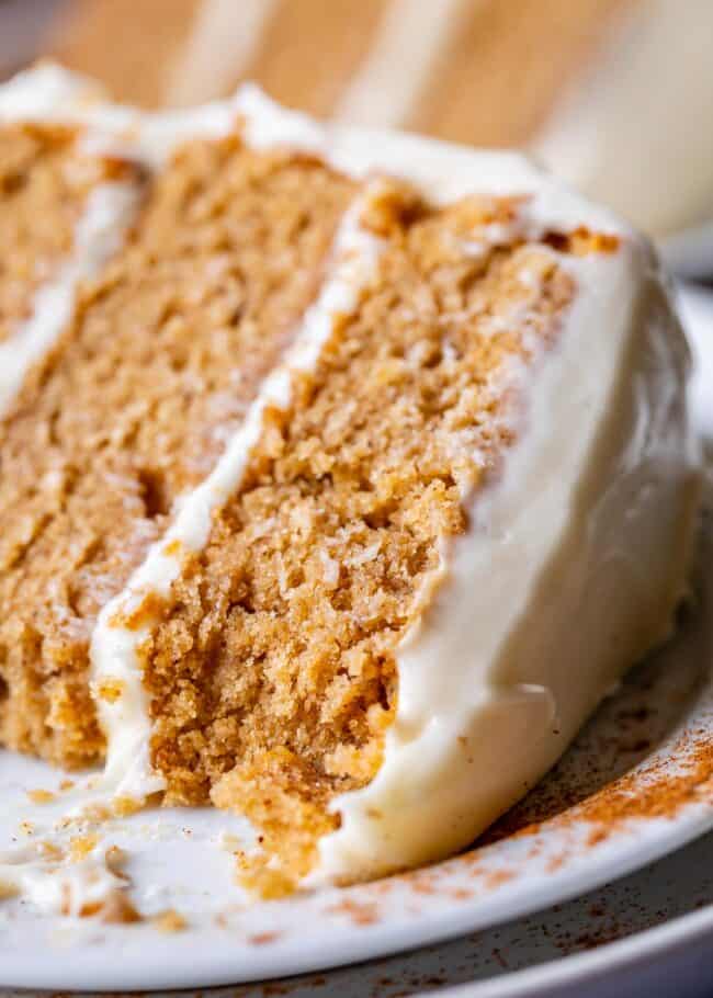 a slice of homemade spice cake with cream cheese frosting from scratch on a plate with bites taken out of it. 