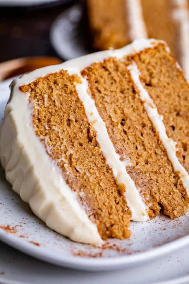 slice of 3 layer homemade spice cake with cream cheese frosting on a plate.