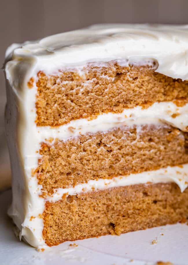 homemade 3 layer spice cake with cream cheese frosting with slices cut out of it. 