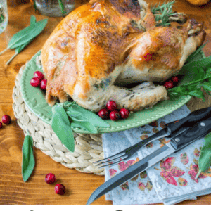 A golden roasted turkey garnished with herbs and cranberries sits on a green platter, surrounded by fresh flowers, pumpkins, and festive fall decor on a wooden table. Text below reads: Sage Butter Roasted Turkey centerpiece.