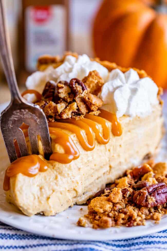 slice of easy no bake pumpkin cheesecake with caramel drizzle, pecans, and whipped cream.