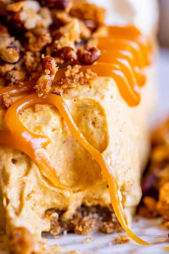 close up shot of a bite taken out of no bake pumpkin cheesecake with caramel sauce.