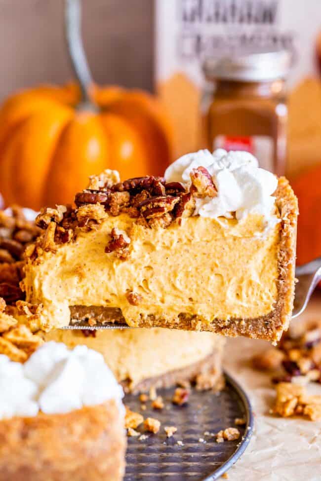 no bake pumpkin cheesecake with whipped cream and pecan crumble being lifted from the pan.