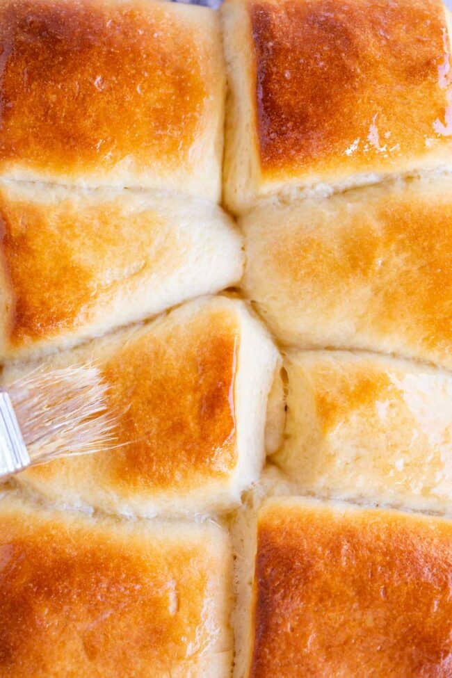 parker house rolls in a pan being brushed with butter.