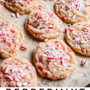 Freshly baked sugar cookies topped with crushed peppermint candies and festive candy canes are arranged on a parchment-lined baking sheet. Text at the bottom reads: Peppermint Crunch Sugar Cookies.