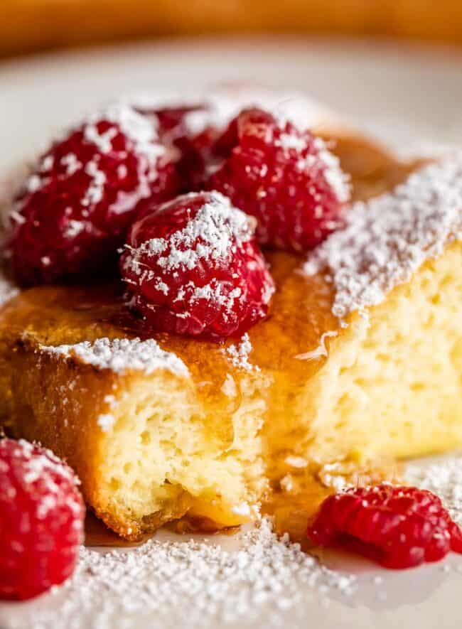a fluffy german pancake with syrup, powdered sugar, and raspberries.