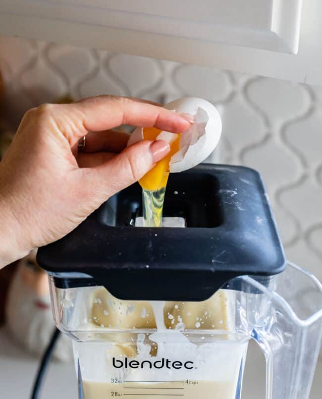 cracking an egg into batter that's in a blender.